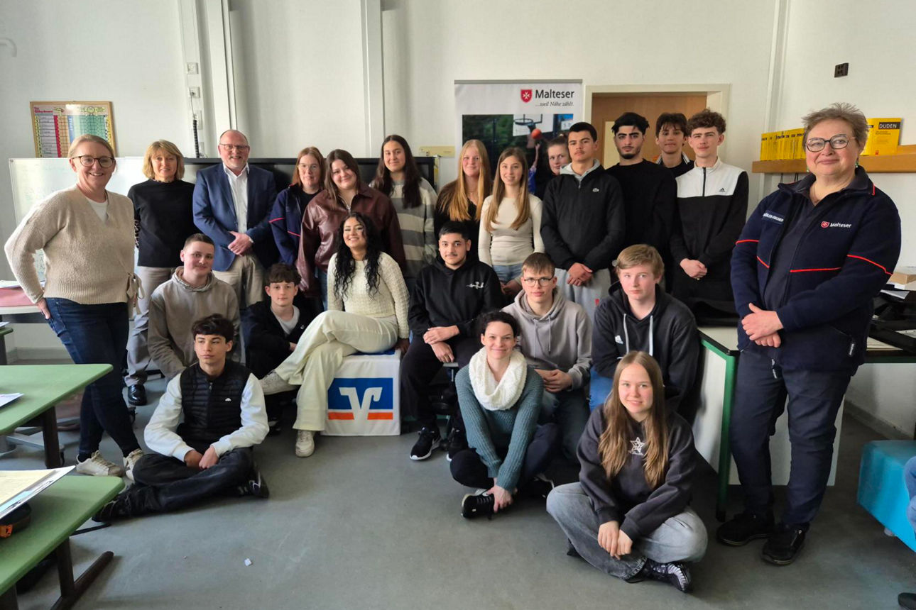 Auf dem Bild ist eine größere Gruppe von Jugendlichen und Erwachsenen in einem Klassenraum zu sehen.