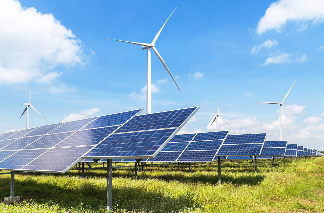 Windräder und Solarpannels auf grüner Wiese vor blauem Himmel