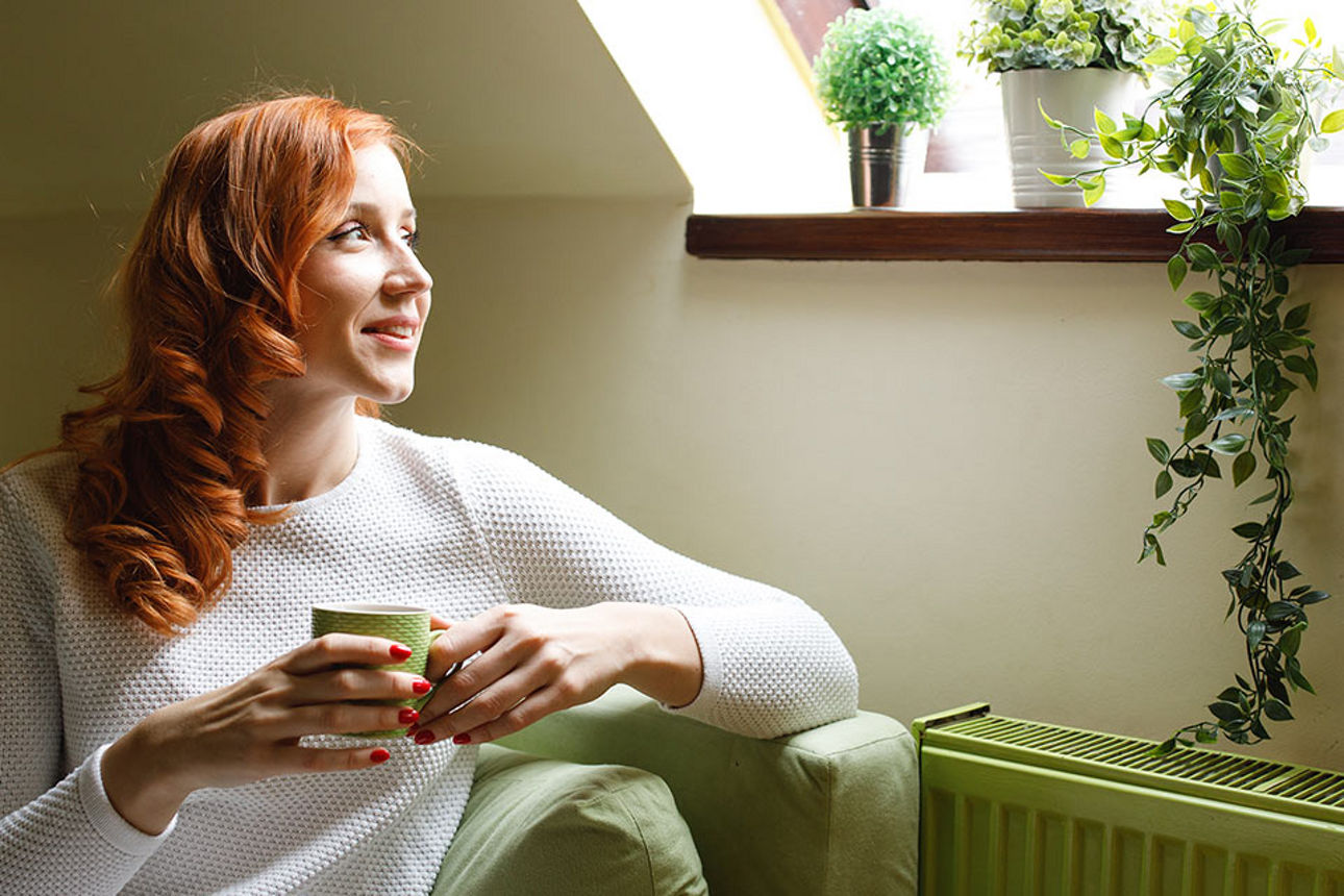 Eine Frau mit einer Tasse sieht durch ein Fenster