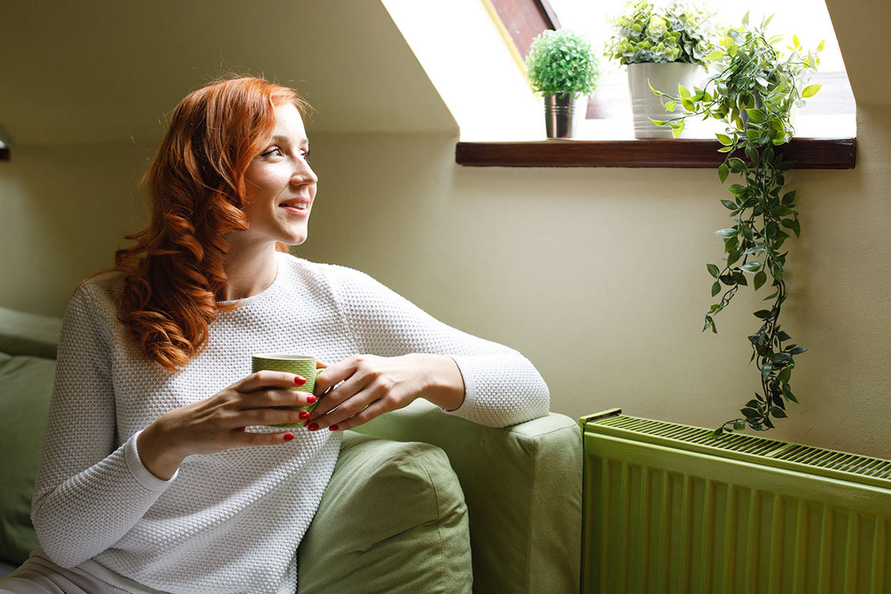 Eine Frau sitzt auf einem grünen Sofa in einer Dachwohnung und sieht zum Dachfenster hinaus.