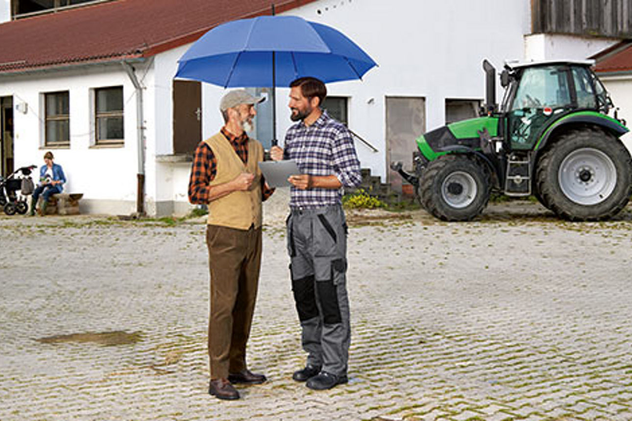Zwei Männer geschützt unter einem Schirm auf dem Hof eines Landwirtschaftsbetriebs