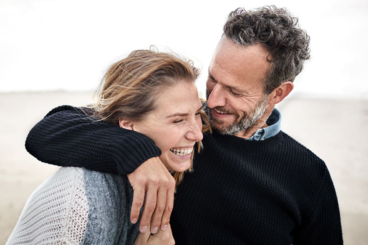 Ein lachendes Pärchen umarmt sich am Strand