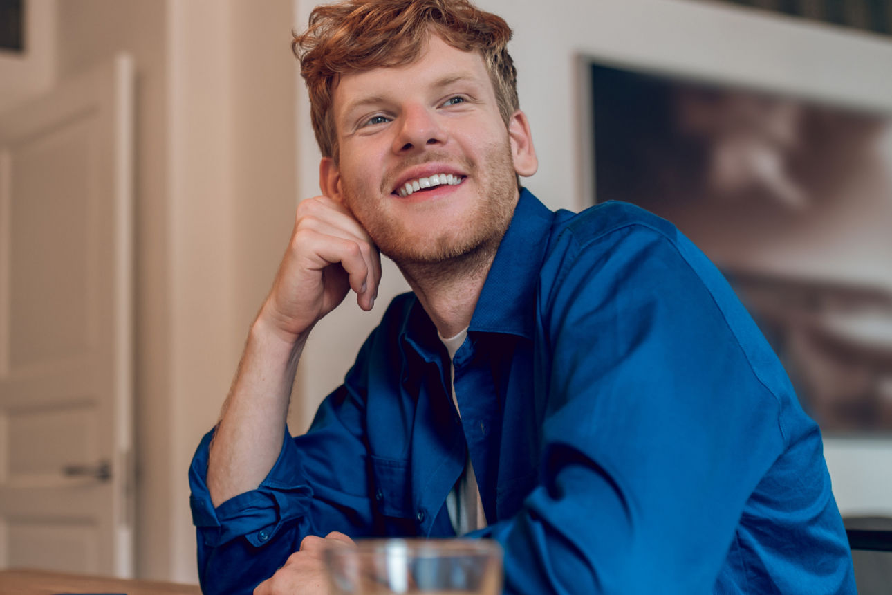 Person sitzt am Tisch vor einem Laptop und stützt den Kopf auf die Hand, daneben ein Glas Orangensaft.