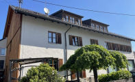 Zweistöckiges Haus mit Dachgauben und Bäumen im Vorgarten.
