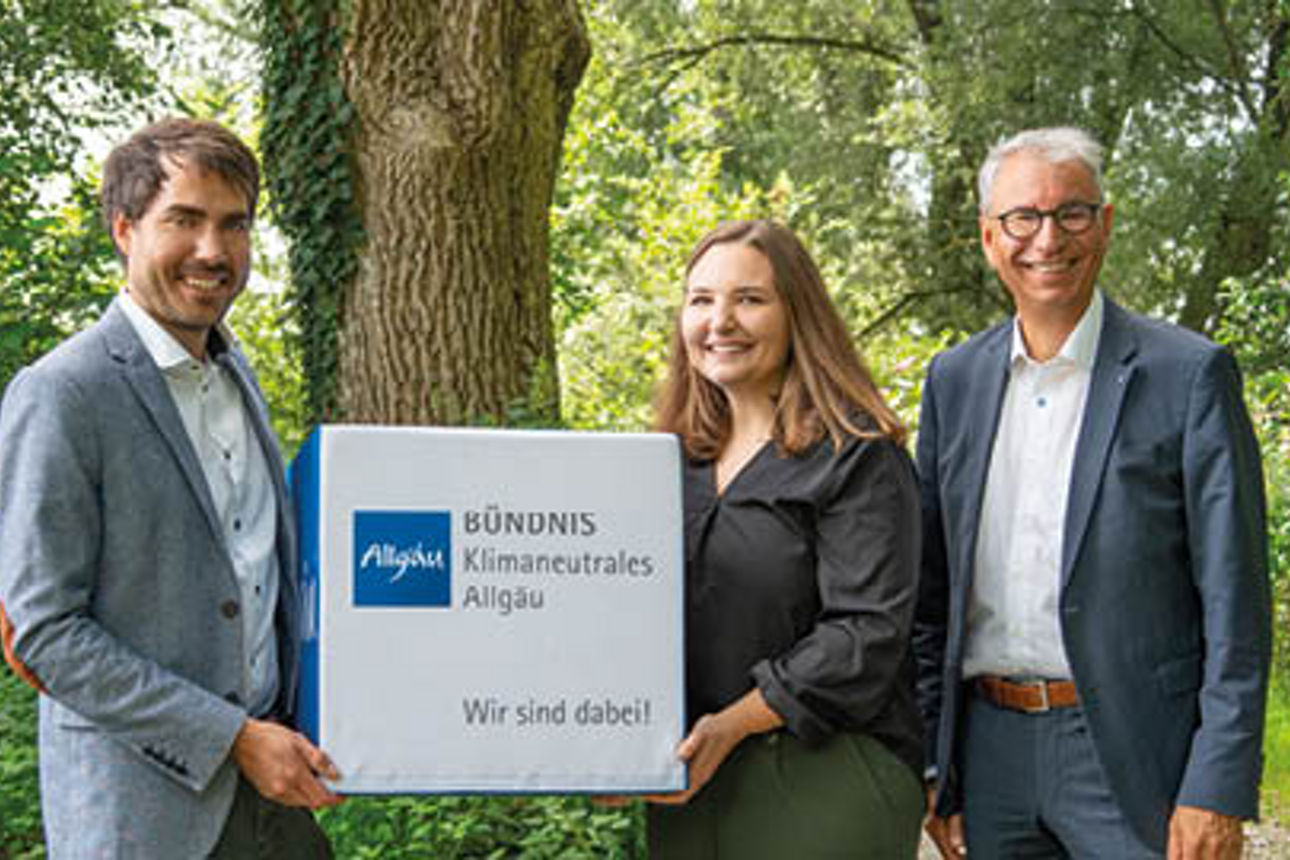 Ein Mann und eine Frau halten einen Würfel in die Höhe mit der Aufschrift "Bündnis klimaneutrales Allgäu. Wir sind dabei!". Daneben steht ein weiterer Mann. Sie stehen im Grünen.