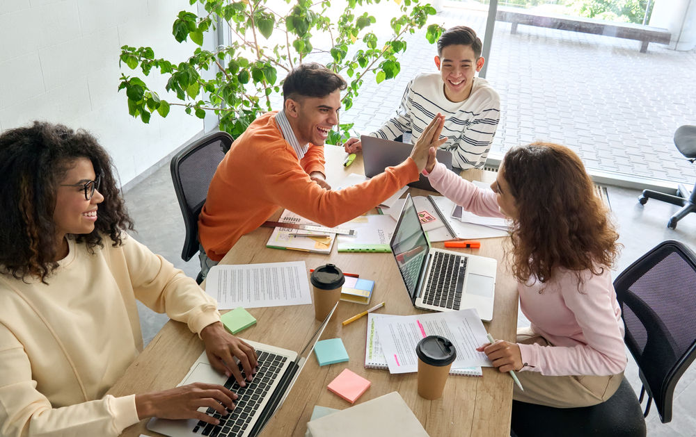 Ein junges Team sitzt an einem Tisch voller Unterlagen und arbeitet zusammen an einem Projekt