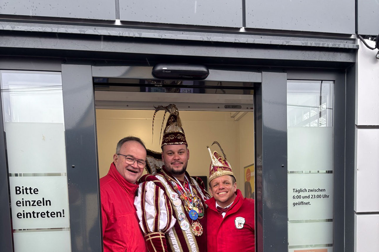 Vorstand Martin Leis und KG-Vorsitzender Mario Müller mit Prinz Hasi in der Mitte. Sie stehen im Eingang zum Geldautomaten.