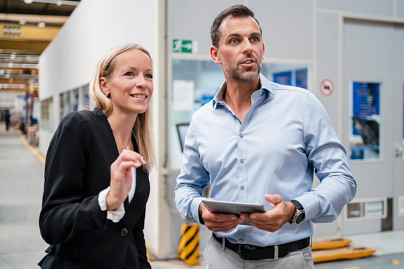 Eine Frau und ein Mann bei einer Besprechung in einer Werkhalle.