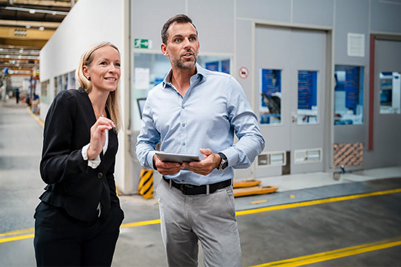 Mann und Frau stehen in Produktionshalle