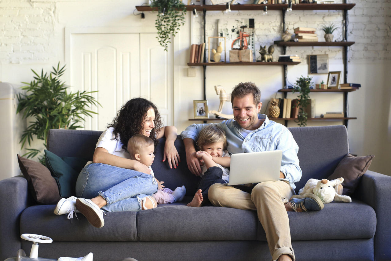 eine junge Familie sitzt auf dem Sofa und schaut auf einen Laptop