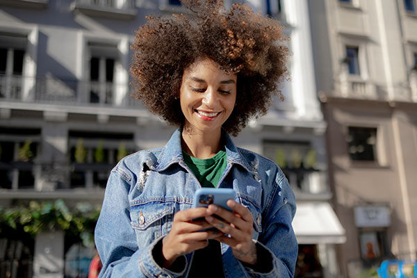 Junge lächende Frau stehend mit Handy in der Hand