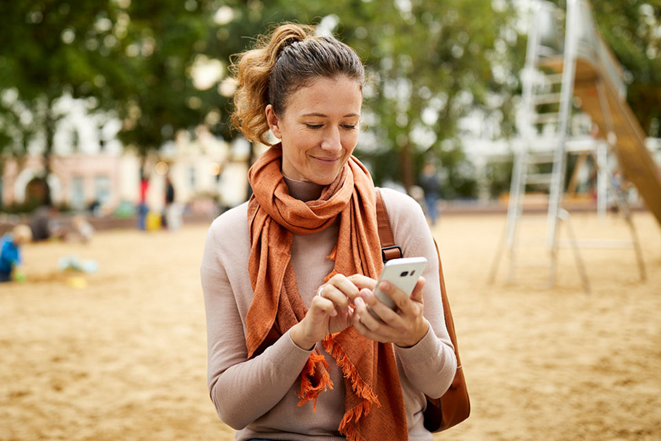 Eine Frau auf einem Spielplatz tippt etwas in ihr Handy