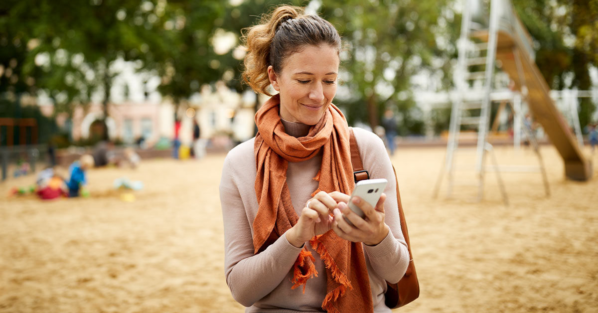 Frau ist auf dem Spielplatz und tippt etwas in ihr Smartphone ein