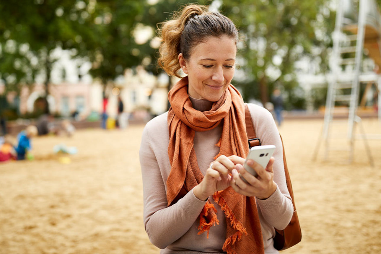 Frau ist auf dem Spielplatz und tippt etwas in ihr Smartphone ein