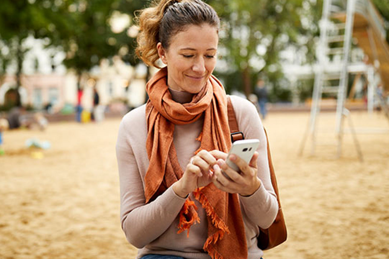 Eine Frau auf einem Spielplatz tippt etwas in ihr Handy