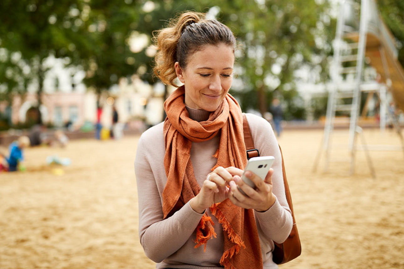 Eine Frau sitzt auf einem Spielplatz mit einem Handy in der Hand