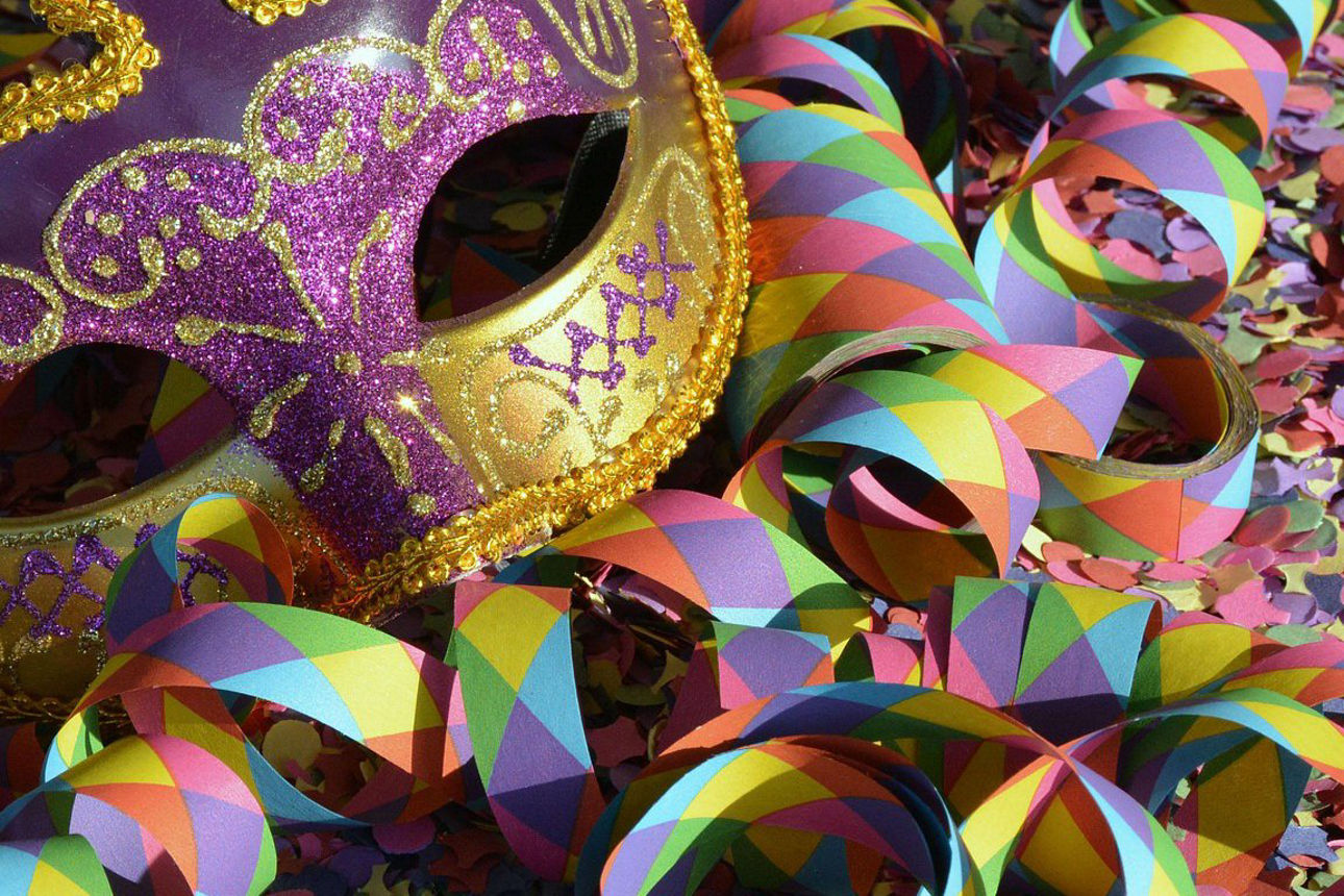 Eine venezianische Maske liegt auf Luftschlangen und Konfetti.