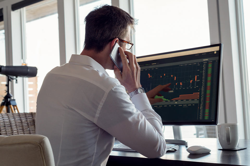 Ein Mann schaut auf seinen Computerbildschirm und telefoniert