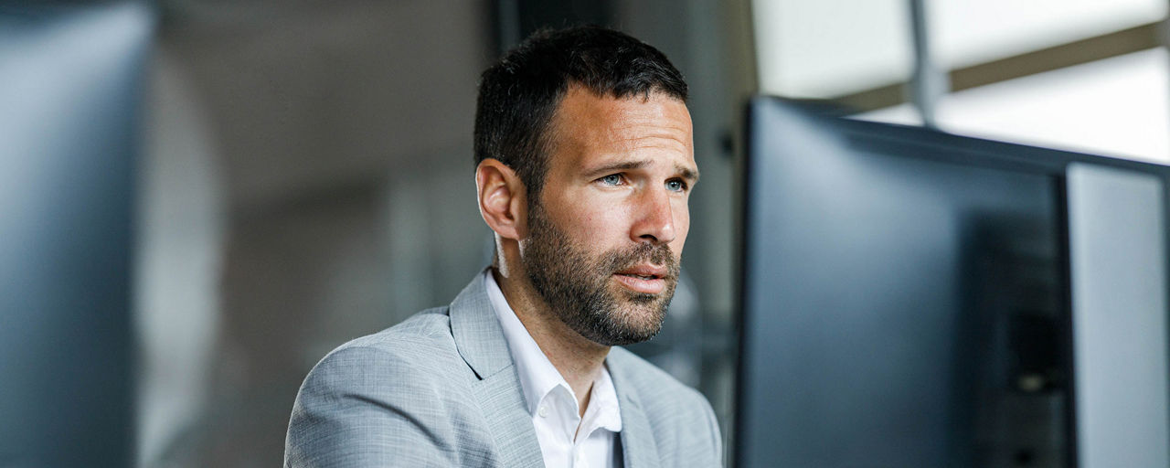Ein Mann sitzt am Schreibtisch und schaut auf einen Computerbildschirm