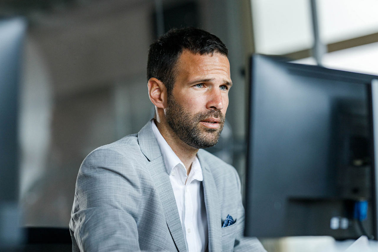 Ein Mann sitzt am Schreibtisch und schaut auf einen Computerbildschirm