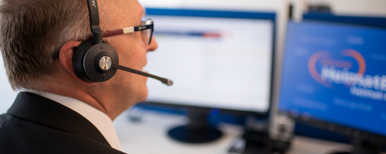 Mitarbeiter mit Headset schaut auf zwei Bildschirme