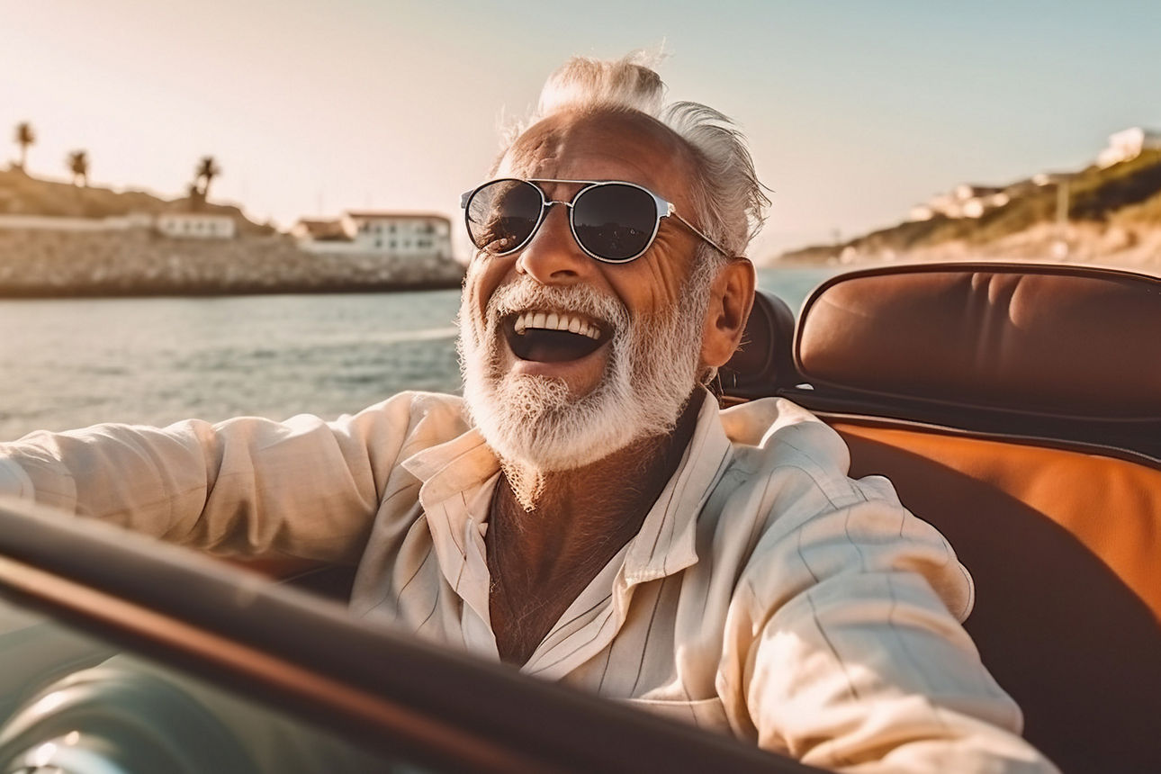 Älterer Herr mit Sonnenbrille fährt im Cabrio in den Sonnenuntergang