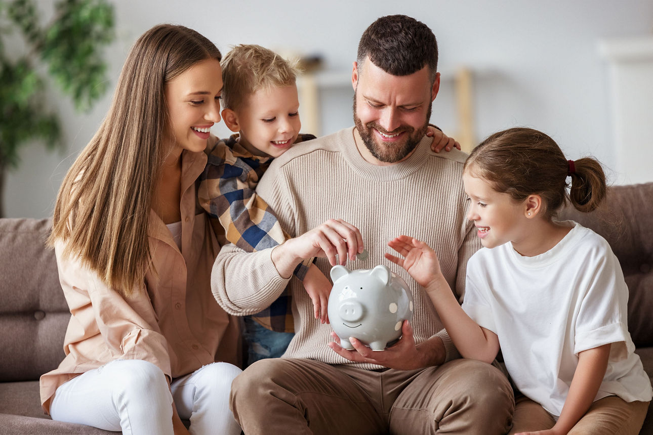 Eltern füttern gemeinsam mit ihren zwei Kindern ein Sparschwein mit Geld.