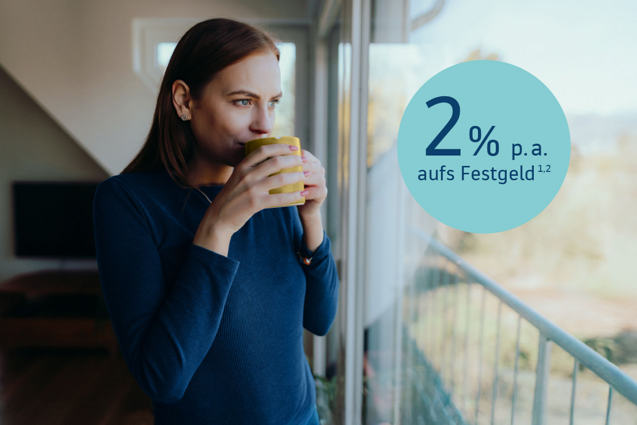 Frau steht mit Kaffeetasse in den Händen am Fenster daneben blauer Kreis mit dem Text: 2% p.a. aufs Festgeld. (hoch1, 2)