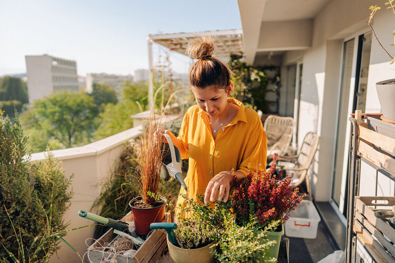 Eine Frau steht auf ihrem Balkon und pflanz Blumen