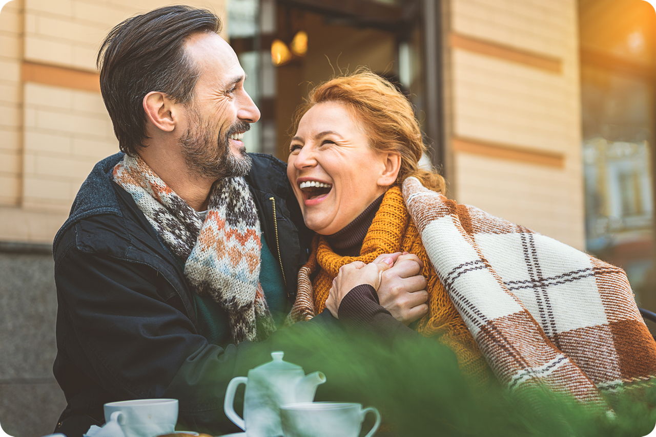Ein Paar sitzt vor einem Kaffee und lacht sich glücklich an