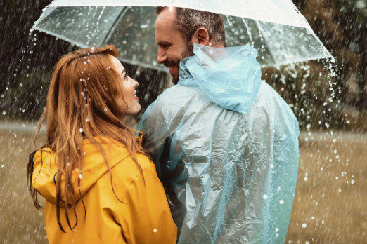 Eine Frau und ein Mann stehem unter einem Regenschirm auf einer Wiese.