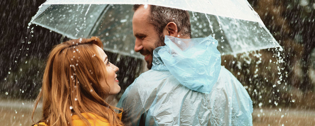 Eine Frau und ein Mann stehem unter einem Regenschirm auf einer Wiese.