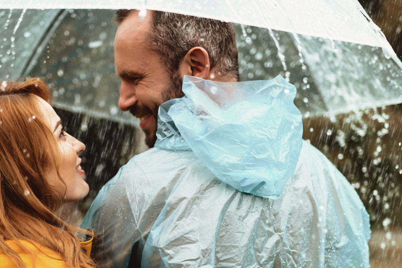 Eine Frau und ein Mann stehem unter einem Regenschirm auf einer Wiese.
