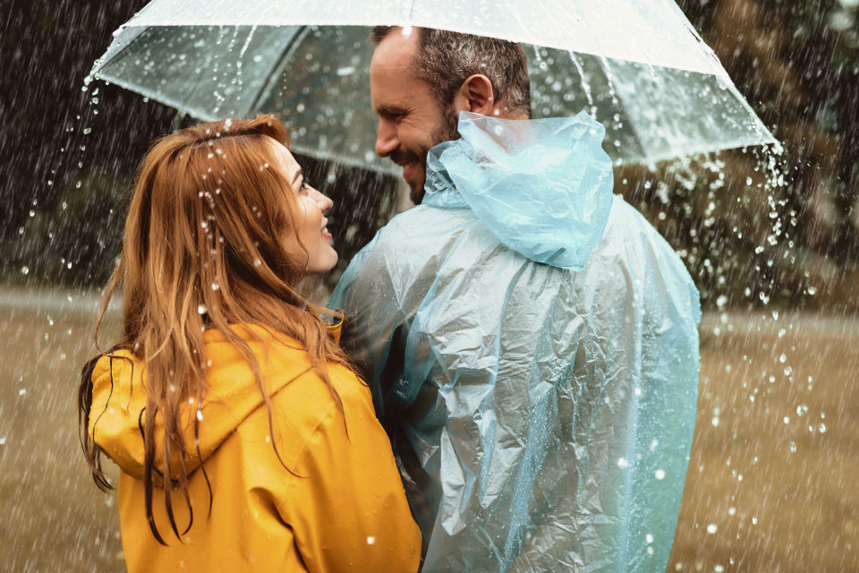 Eine Frau und ein Mann stehem unter einem Regenschirm auf einer Wiese.