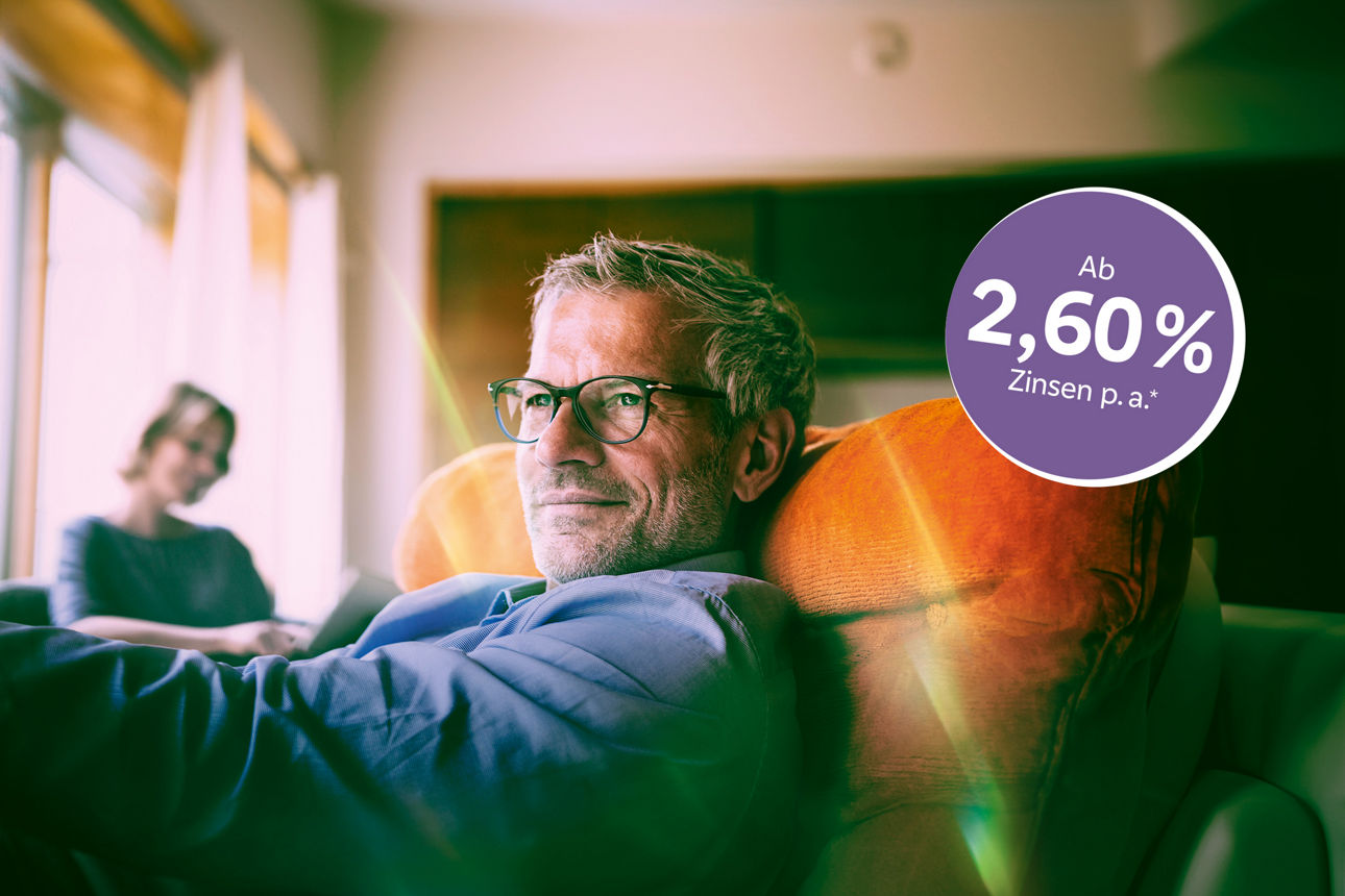 Mann mit Brille sitzt gemütlich auf dem Sofa. Im Hintergrund sieht man noch eine Frau.