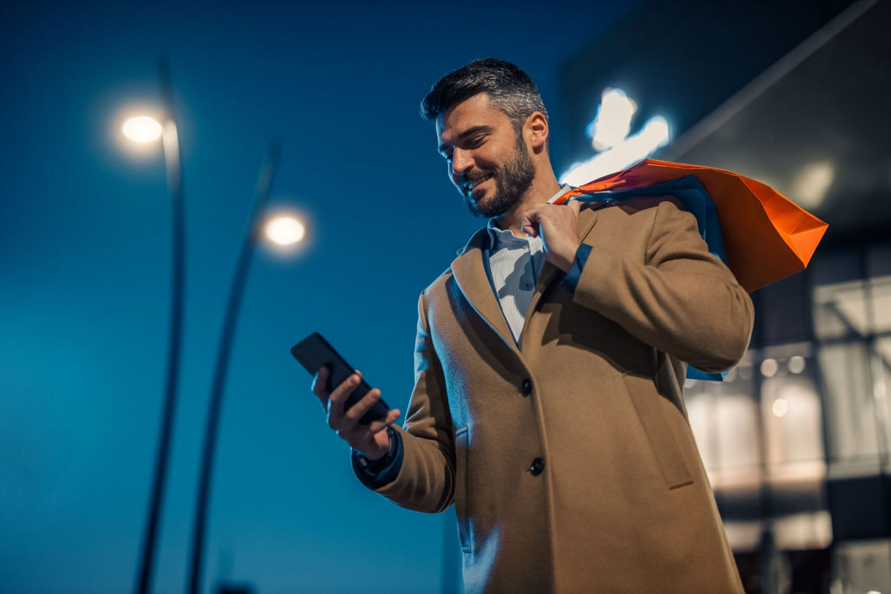 Mann schaut am Abend nach dem Einkaufen auf sein Handy