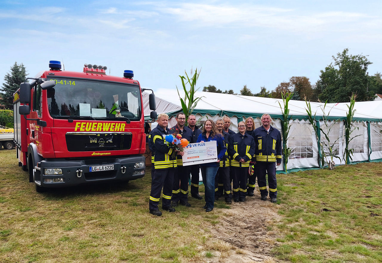 Feuerwehrauto mit Feuerwehrleuten mit einem großer Papierscheck in den Händen