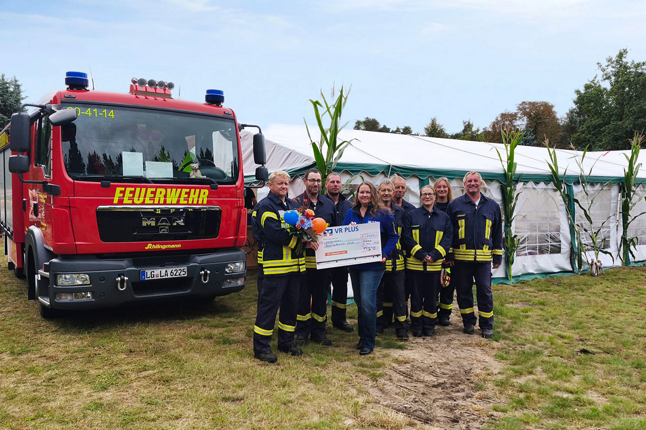 Feuerwehrauto mit Feuerwehrleuten mit einem großer Papierscheck in den Händen