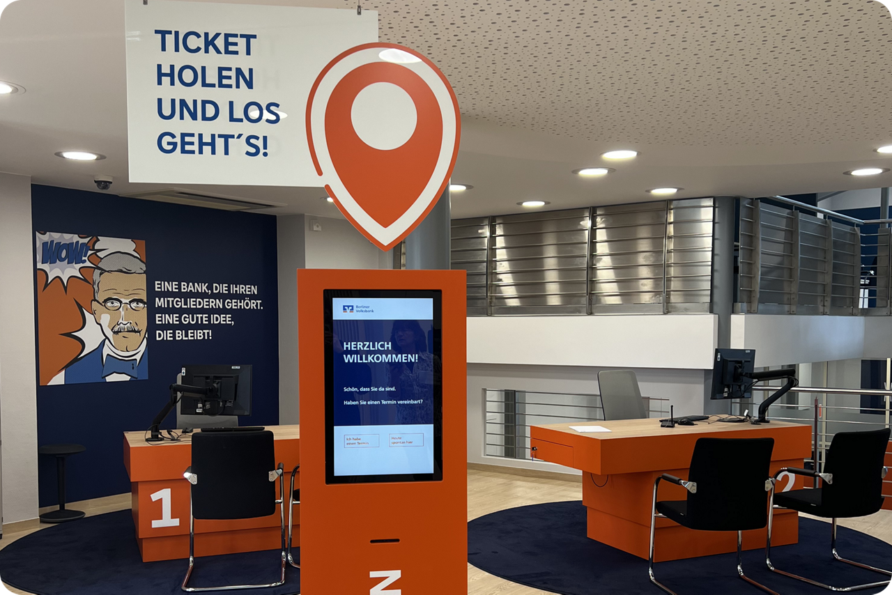 Eingangsbereich der Filiale Rudow mit Monitor und Herzlich willkommen Hinweis