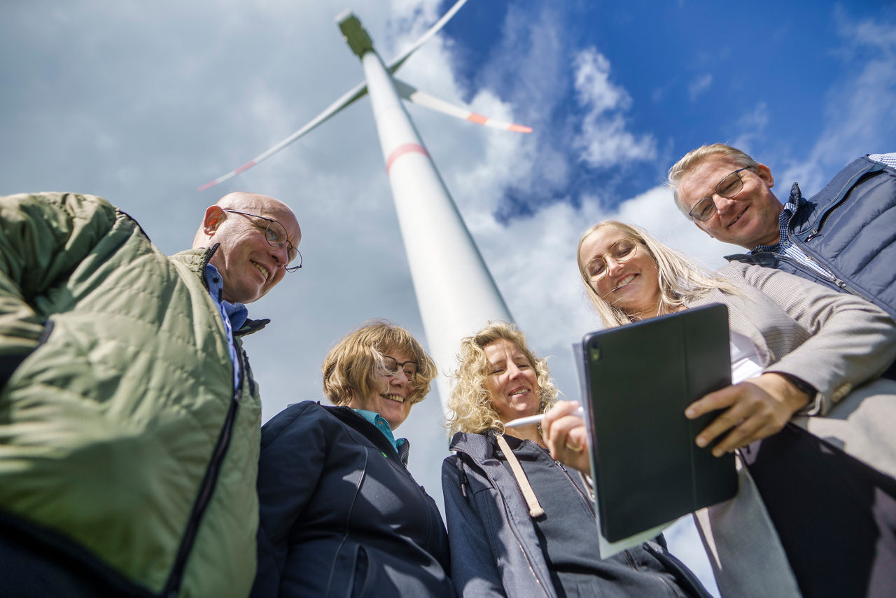 5 Leute stehen vor einer Windmühle und schauen auf ein Tablet