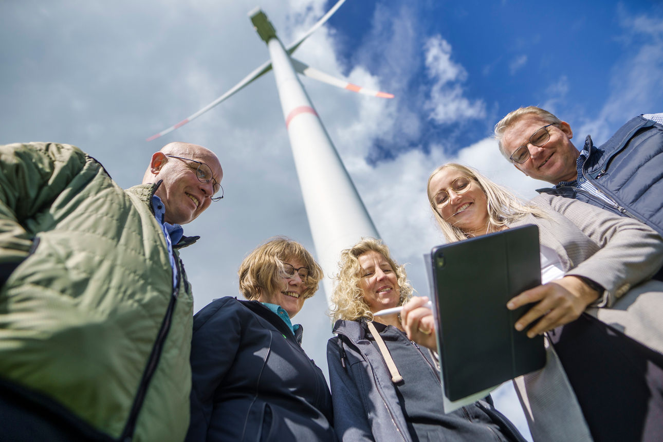 Energiekundenberaterin steht mit vier Kunden vor einer Windmühle.