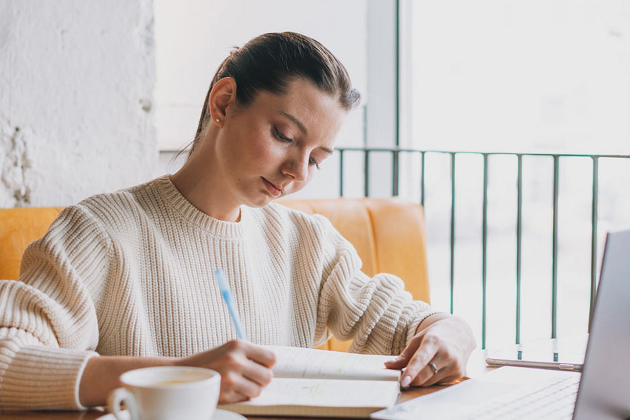 Junge Frau sitzt am Laptop und macht sich Notizen