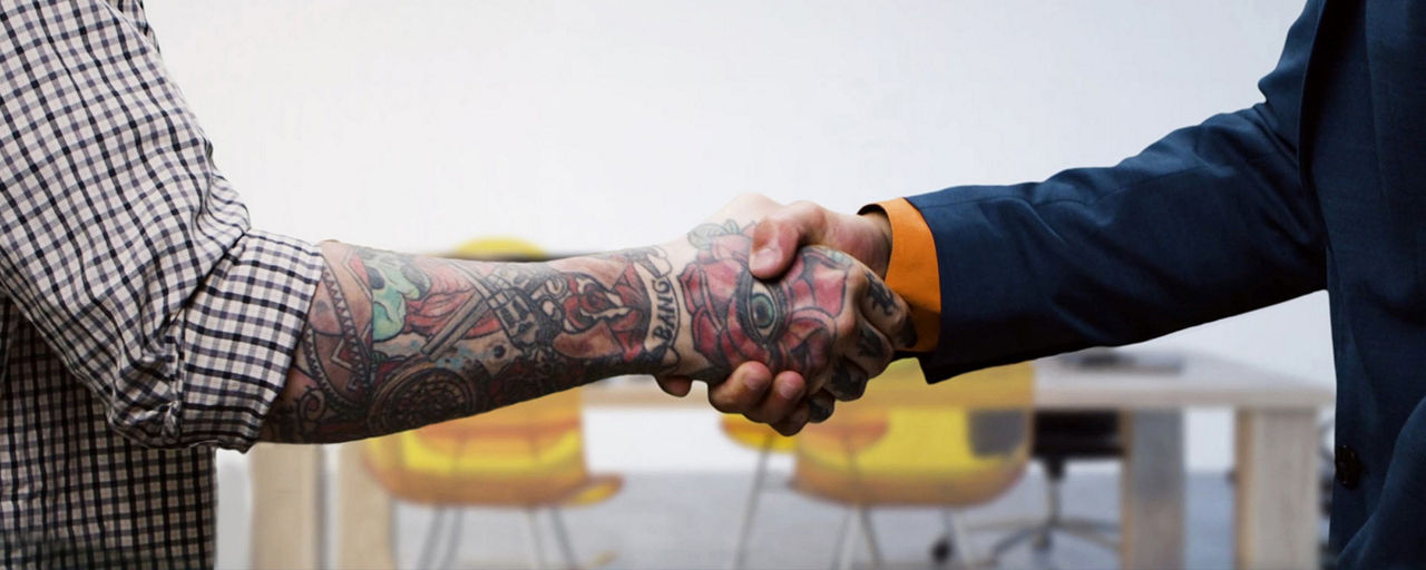Zwei Männer geben sich die Hand, der eine im Anzug, der andere in Hemdsärmeln.