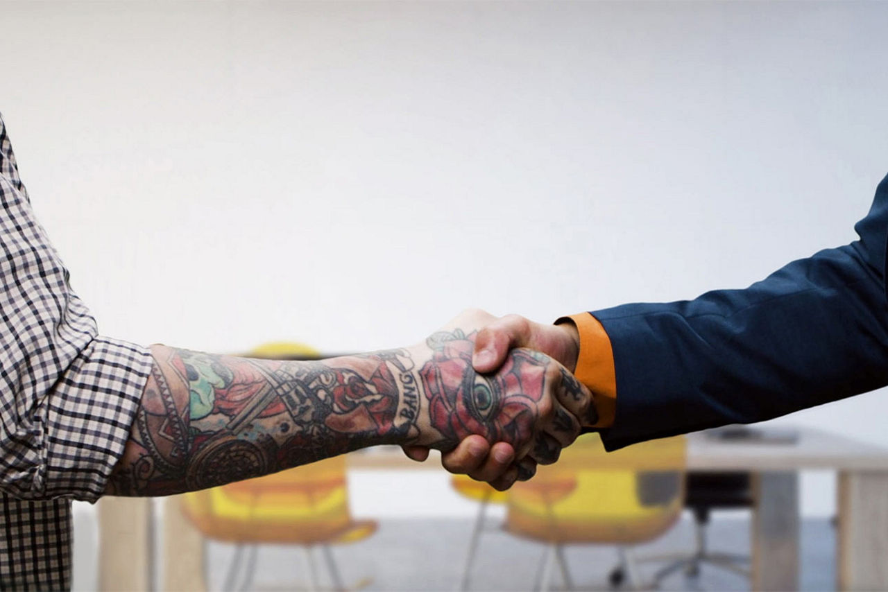 Zwei Männer geben sich die Hand, der eine im Anzug, der andere in Hemdsärmeln.