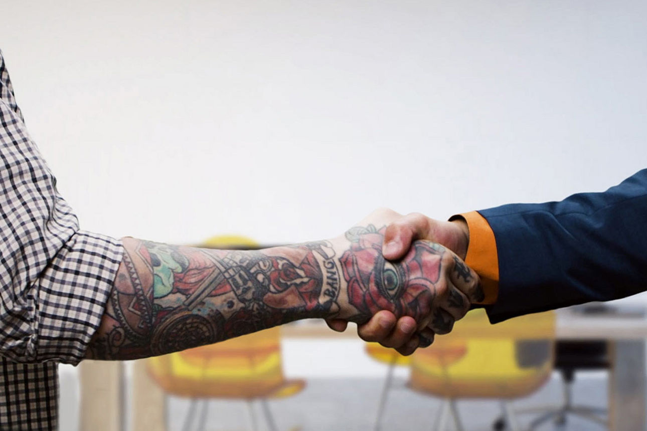 Zwei Männer geben sich die Hand, der eine im Anzug, der andere in Hemdsärmeln.