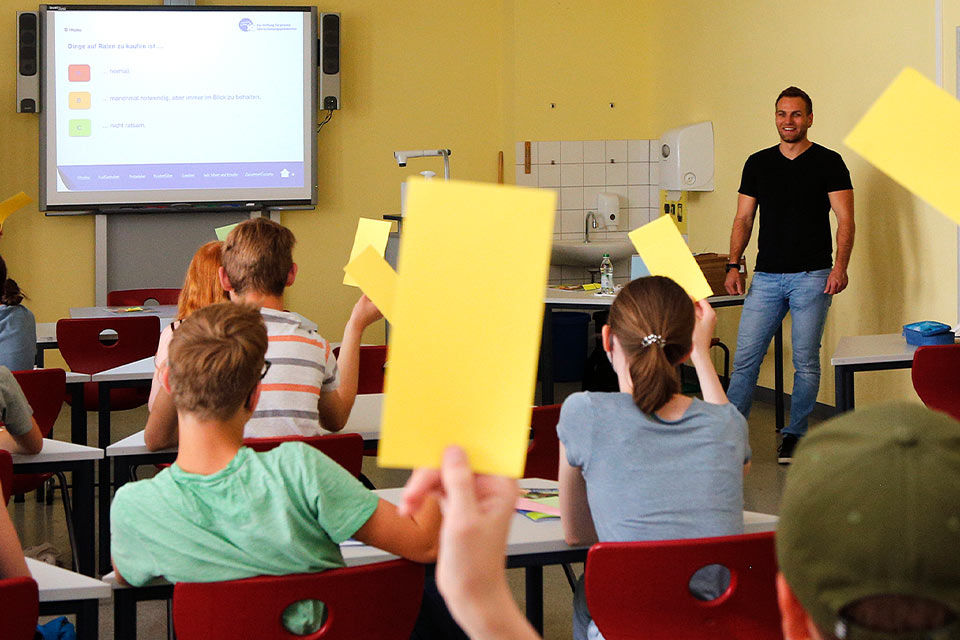 Ein Klassenzimmer mit Schülern die einen Zettel in die Luft halten