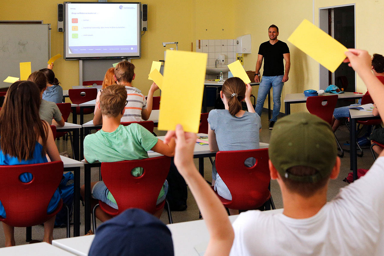 Schulklasse im Unterricht, die Schülerinnen und Schüler heben gelbe Karten hoch