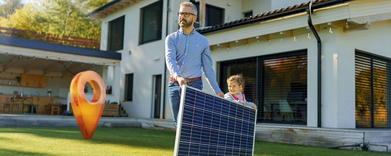 Vater trägt mit seiner Tochter ein Solarpanel im eigenen Garten