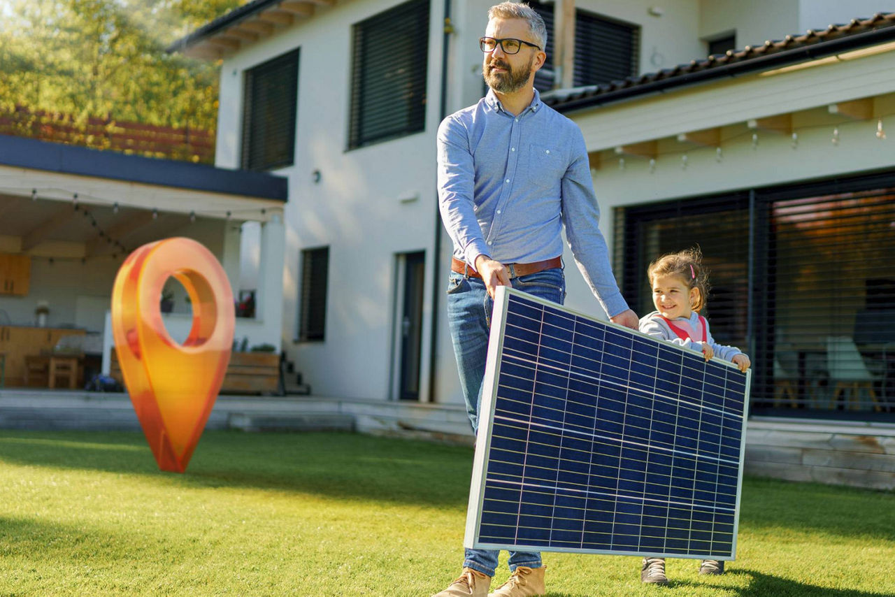 Vater trägt mit seiner Tochter ein Solarpanel im eigenen Garten