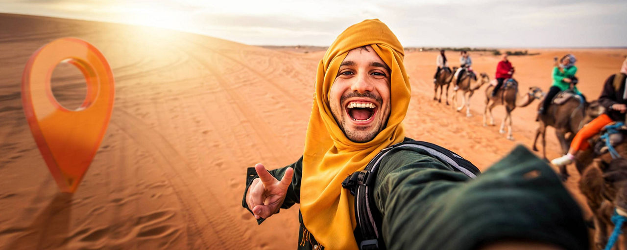 Junger Mann macht in der Wüste auf einem Kamel ein Selfie